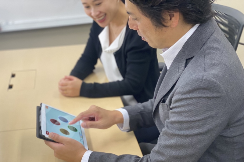 会議室でタブレット端末を使い、CogEvoの画面を見せながら説明