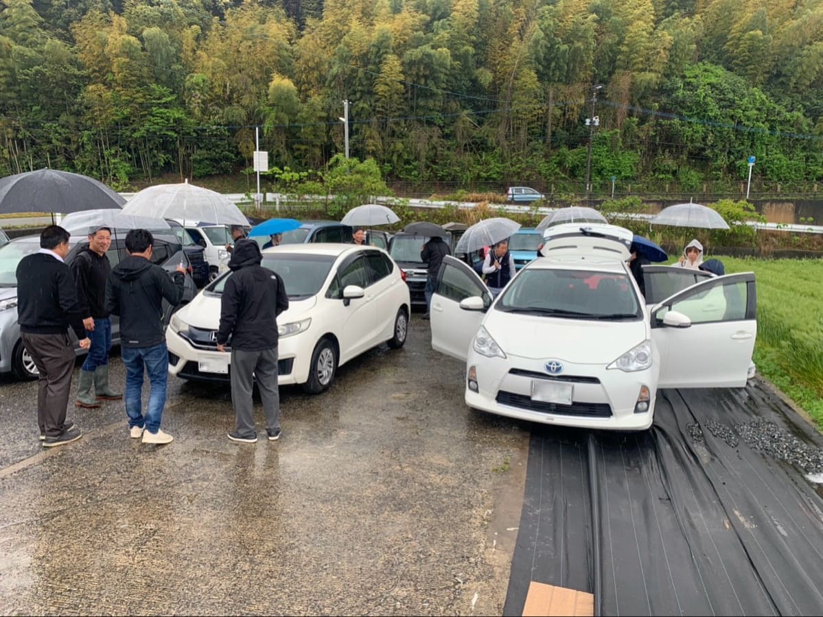 雨のなか複数の関係者が車両を囲んで確認しているハッピーカーズの現場写真