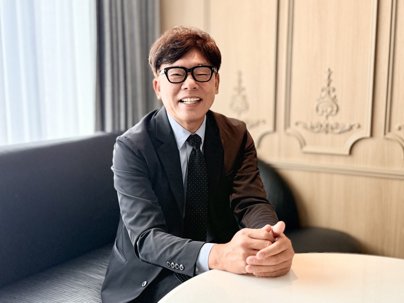 株式会社ハッピーカーズ代表取締役の新佛千治氏が笑顔で着席している写真